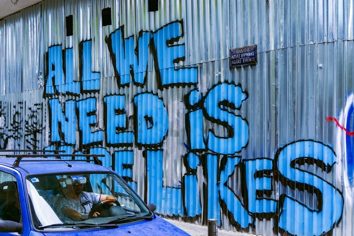 A spray painted sign on a metal wall says All We Need Is More Lik