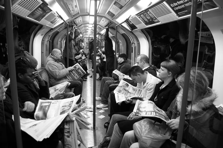 People read the newspaper while riding on a subway car.