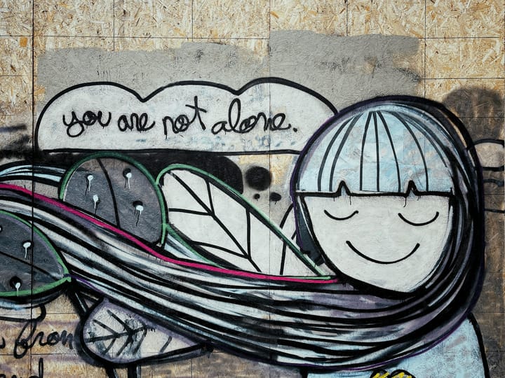 A wall mural shows a person with long hair blowing to the side and the words You Are Not Alone.