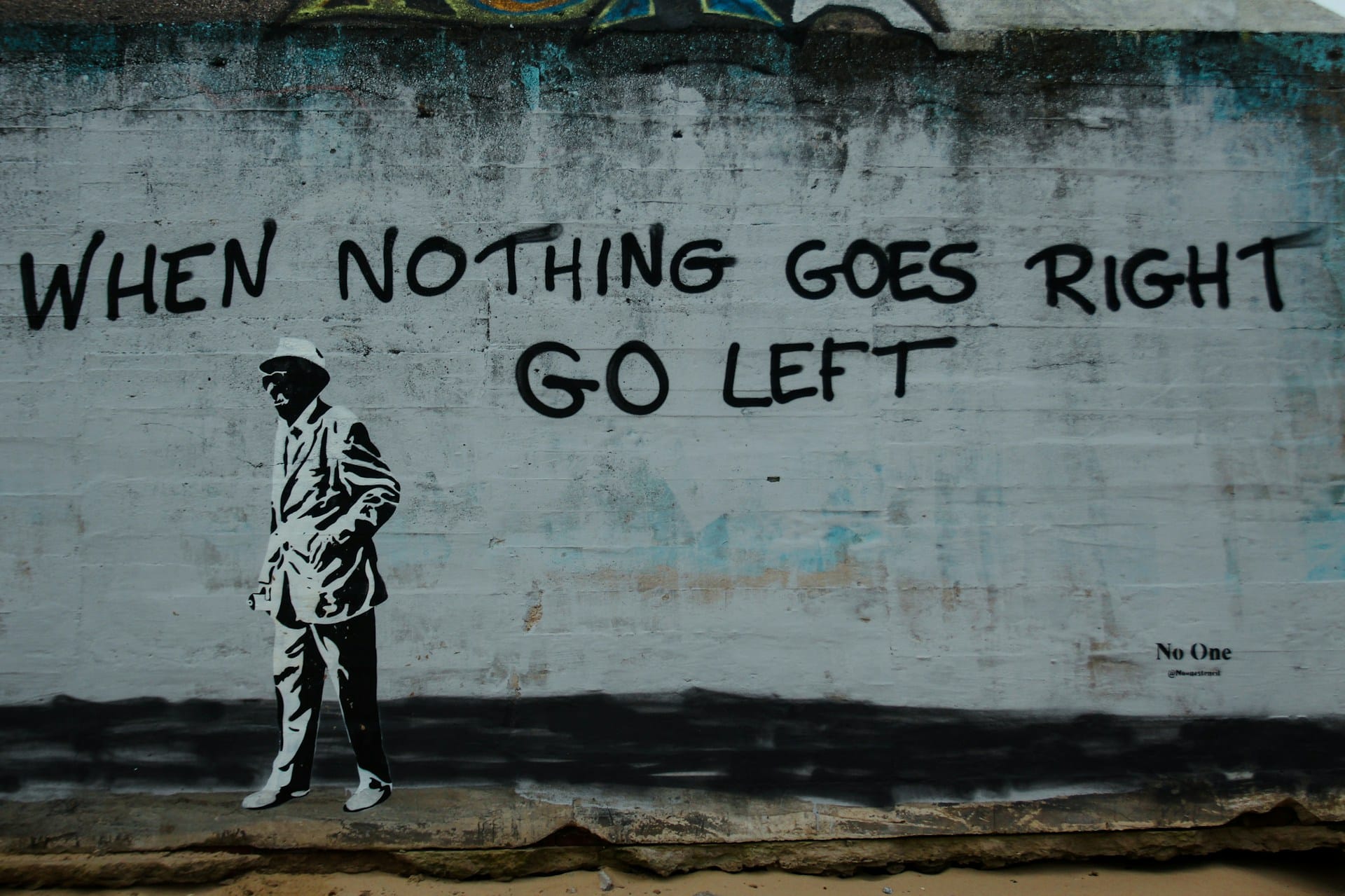 A wall painted with the words When Nothing Goes Right Go Left. A old man in a hat is also painted on the wall. He is walking to the left.